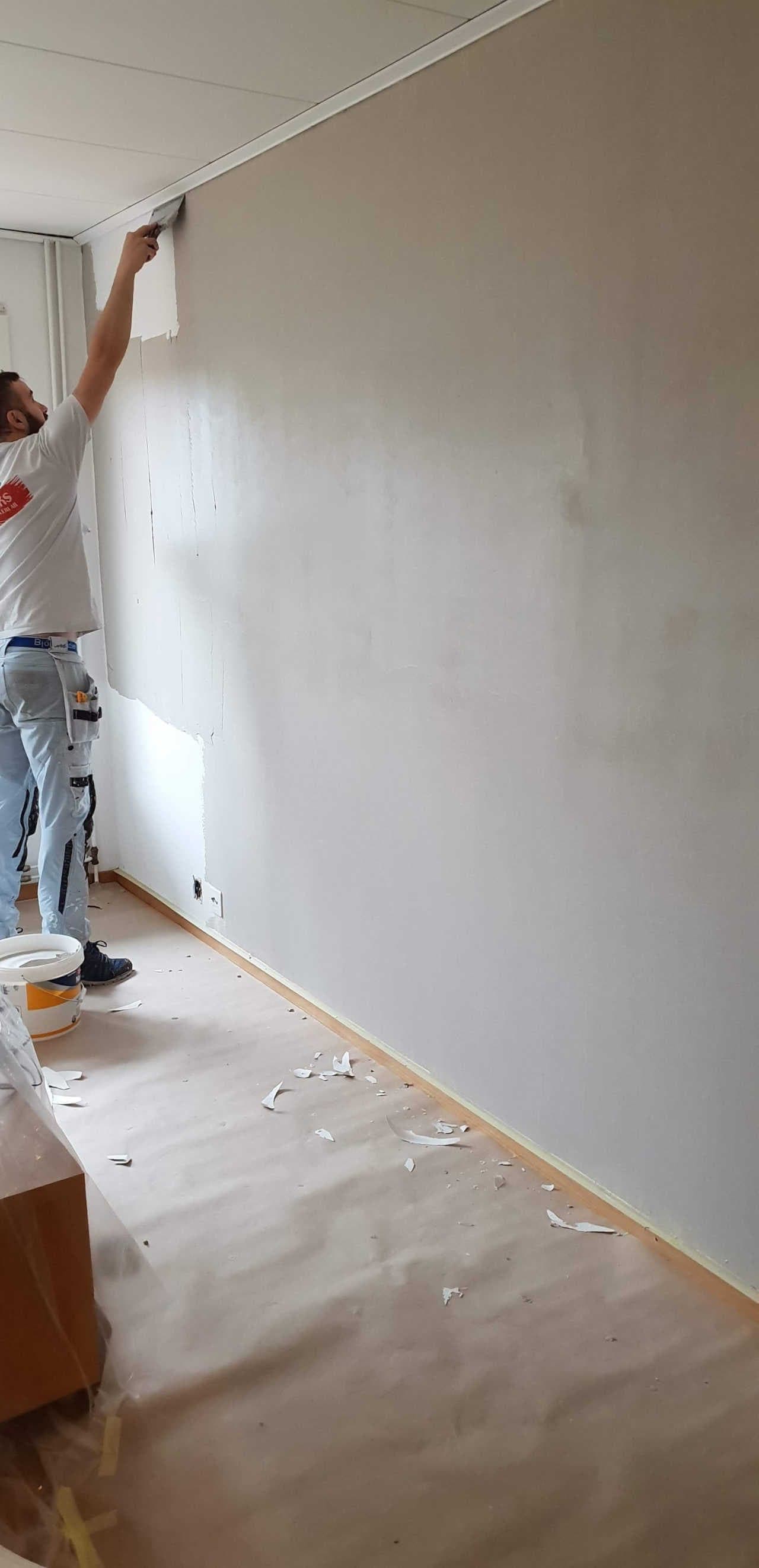 Målare bredspacklar vägg inför ommålning vid renovering