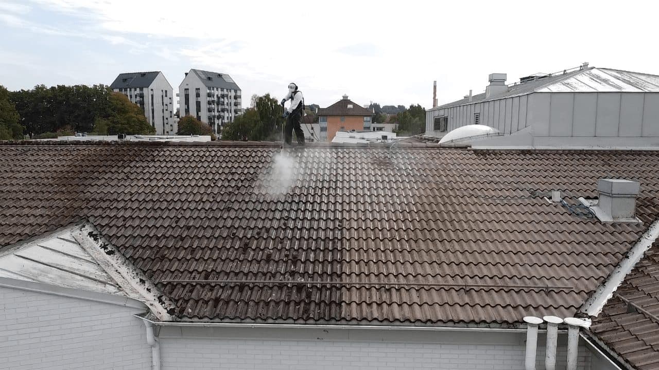 Målare högtryckstvättar tak, flerbostadshus i bakgrunden