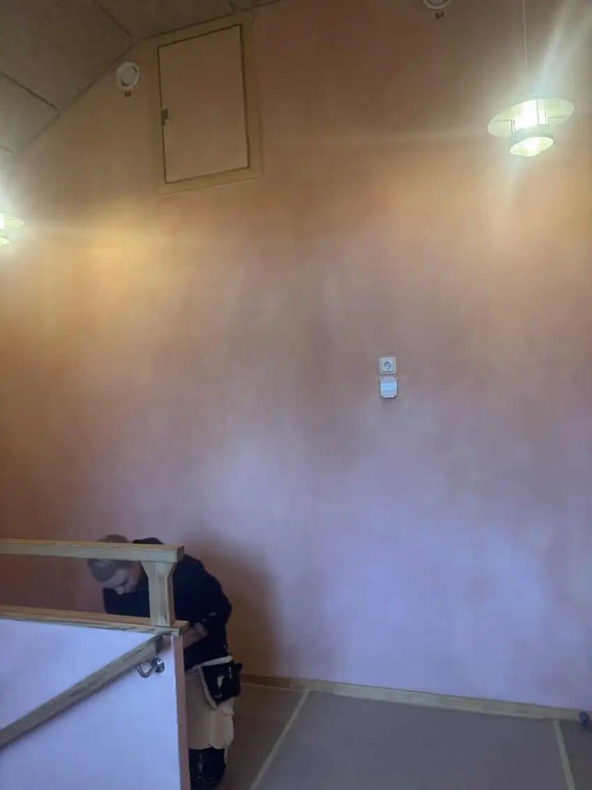 Vägg i varm rosa ton i en trapphall, målare i arbete